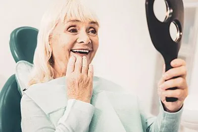 woman checking out her new dentures she got in the mirror